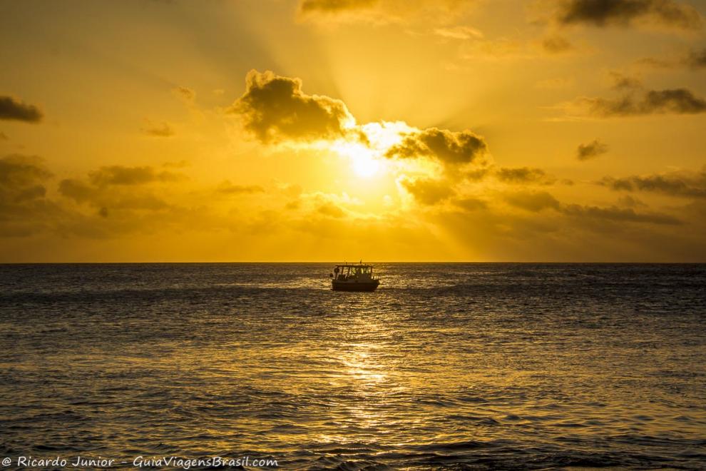 Imagem do por do sol e um barco no mar da Praia da Conceição-.